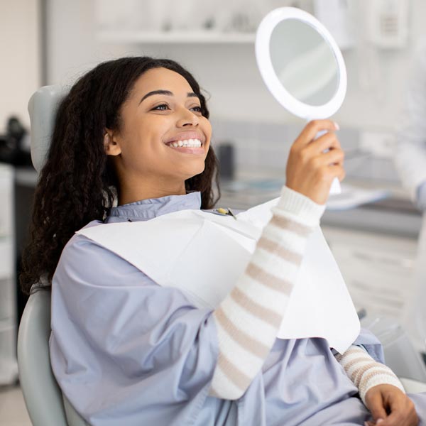 person smiling at hand mirror at dentist